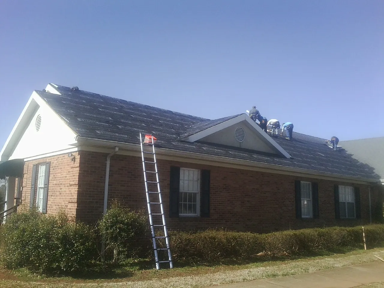 Crew tearing shingles off a brick ranch roof with a ladder set — Metal Roof Repair work by our crew in Herculaneum