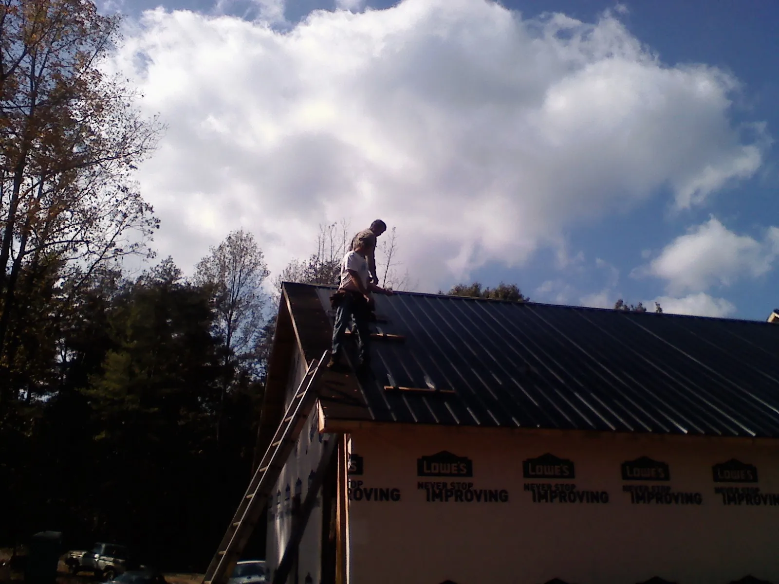 Roofer fastening dark metal panels high against a cloudy sky, from a Roof Inspection job in Herculaneum