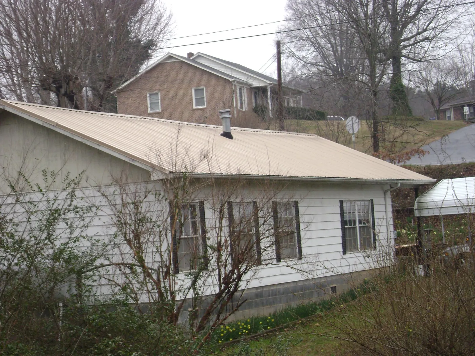 Tan metal roof on a white sided house set into a hillside — Commercial Roofing by Roofing Brothers in Herculaneum