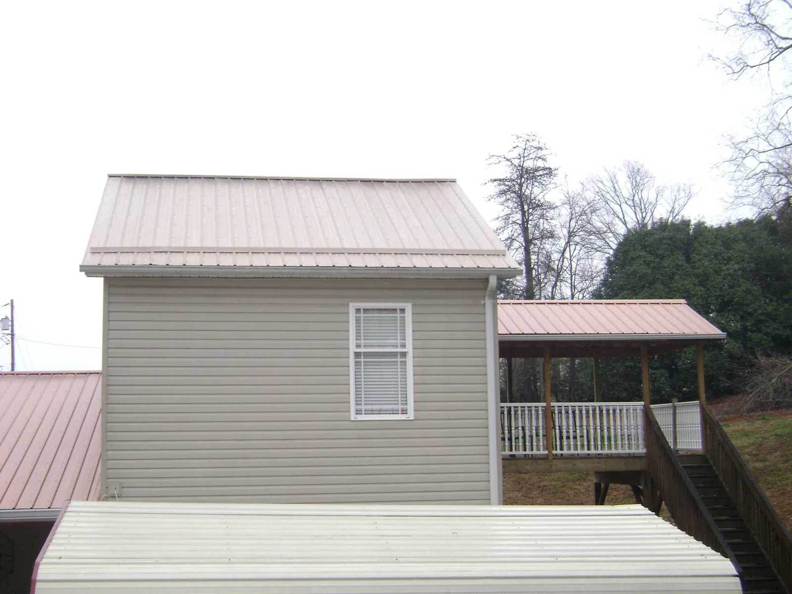 Tan metal roofs on a two story addition and attached porch, from a Roof Replacement job in Herculaneum